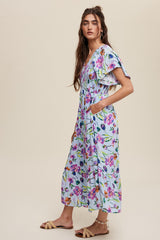 woman wearing a floral maxi dress with short flutter sleeves and pockets, standing against a light background