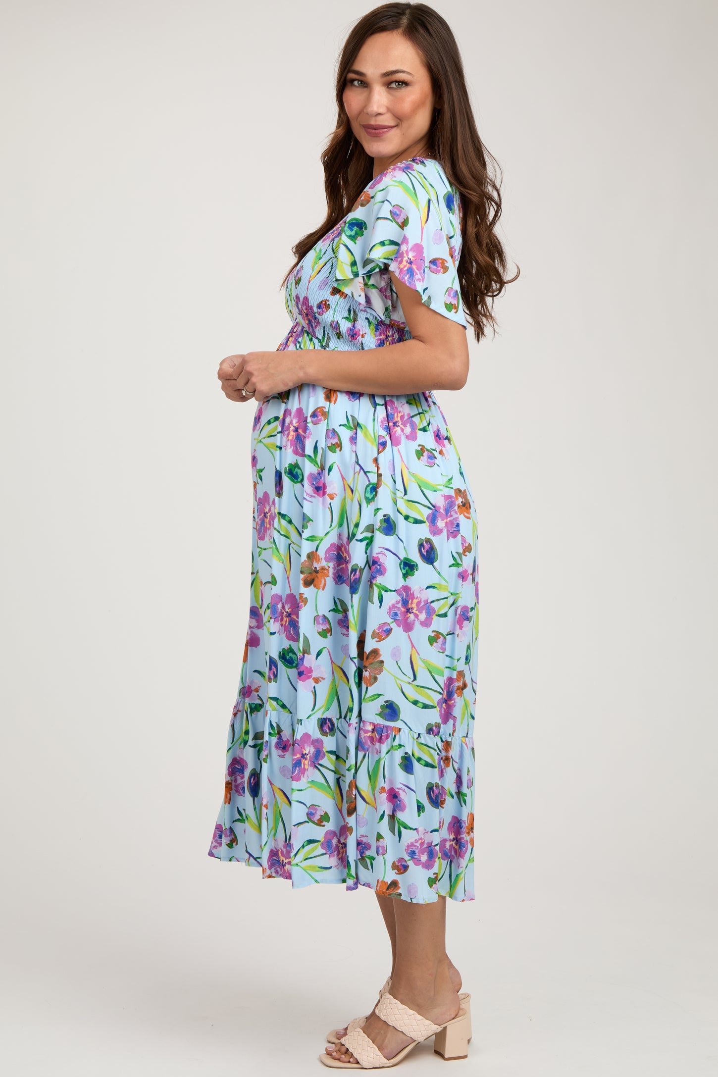 woman wearing a floral short sleeve maternity dress, showing her baby bump, in a light blue color with green accents