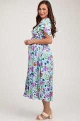 woman wearing a floral short sleeve maternity dress, showing her baby bump, in a light blue color with green accents