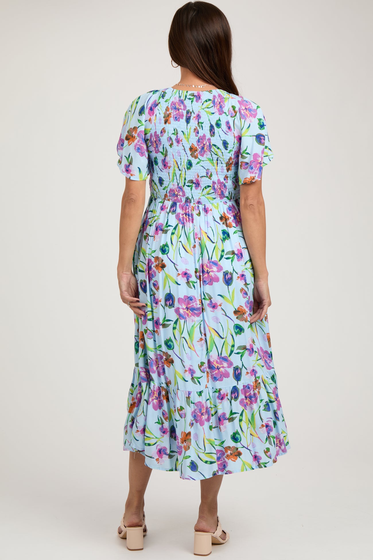 woman wearing a floral print light blue maternity dress with a smocked bodice and short puff sleeves, viewed from the back