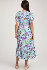 woman wearing a floral print light blue maternity dress with a smocked bodice and short puff sleeves, viewed from the back