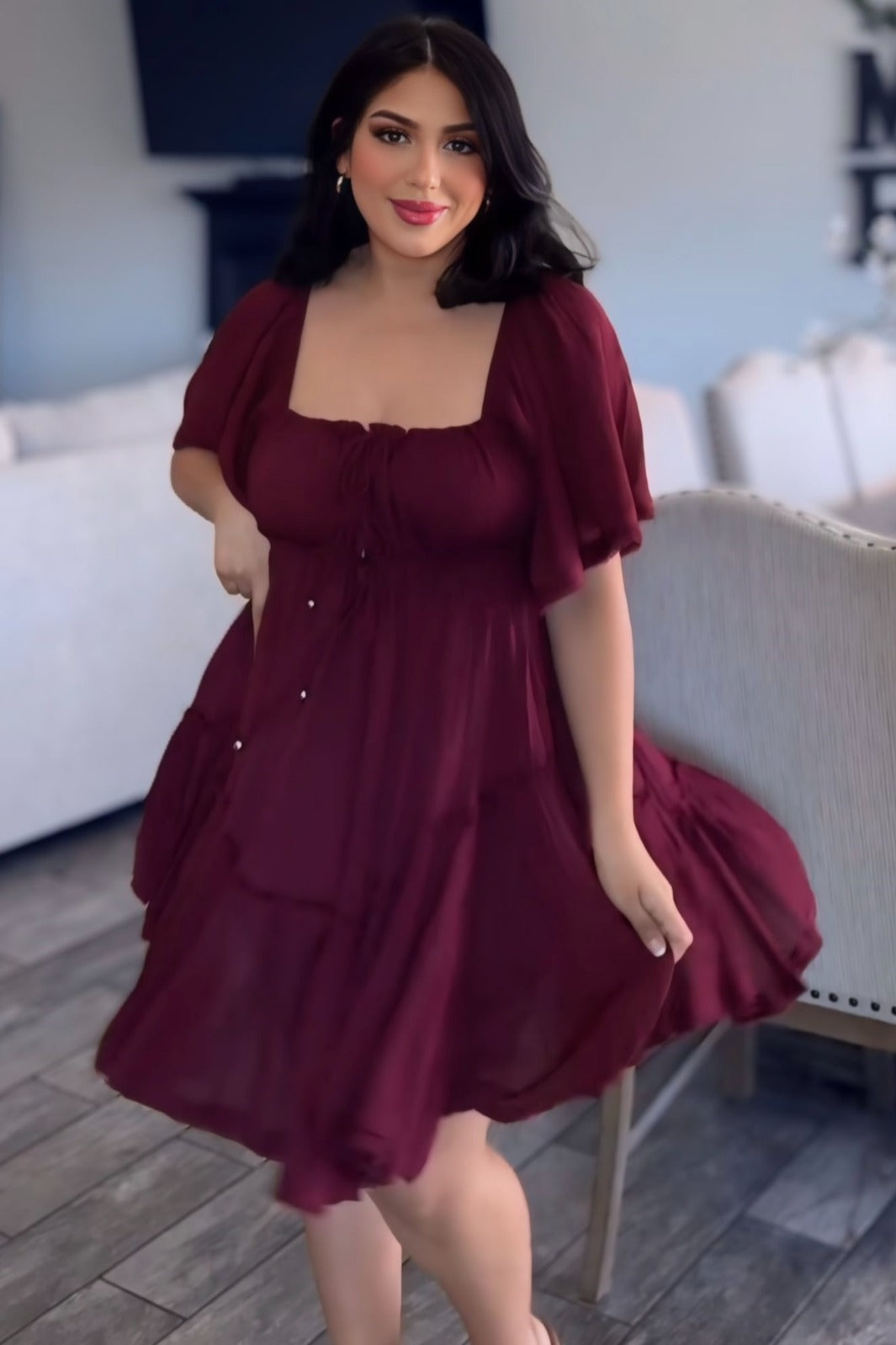 woman wearing a burgundy short tiered dress with a square neckline and flutter sleeves, twirling happily
