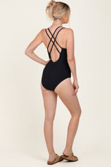 woman wearing a black one-piece swimsuit with crisscross back straps, standing with her back to the camera