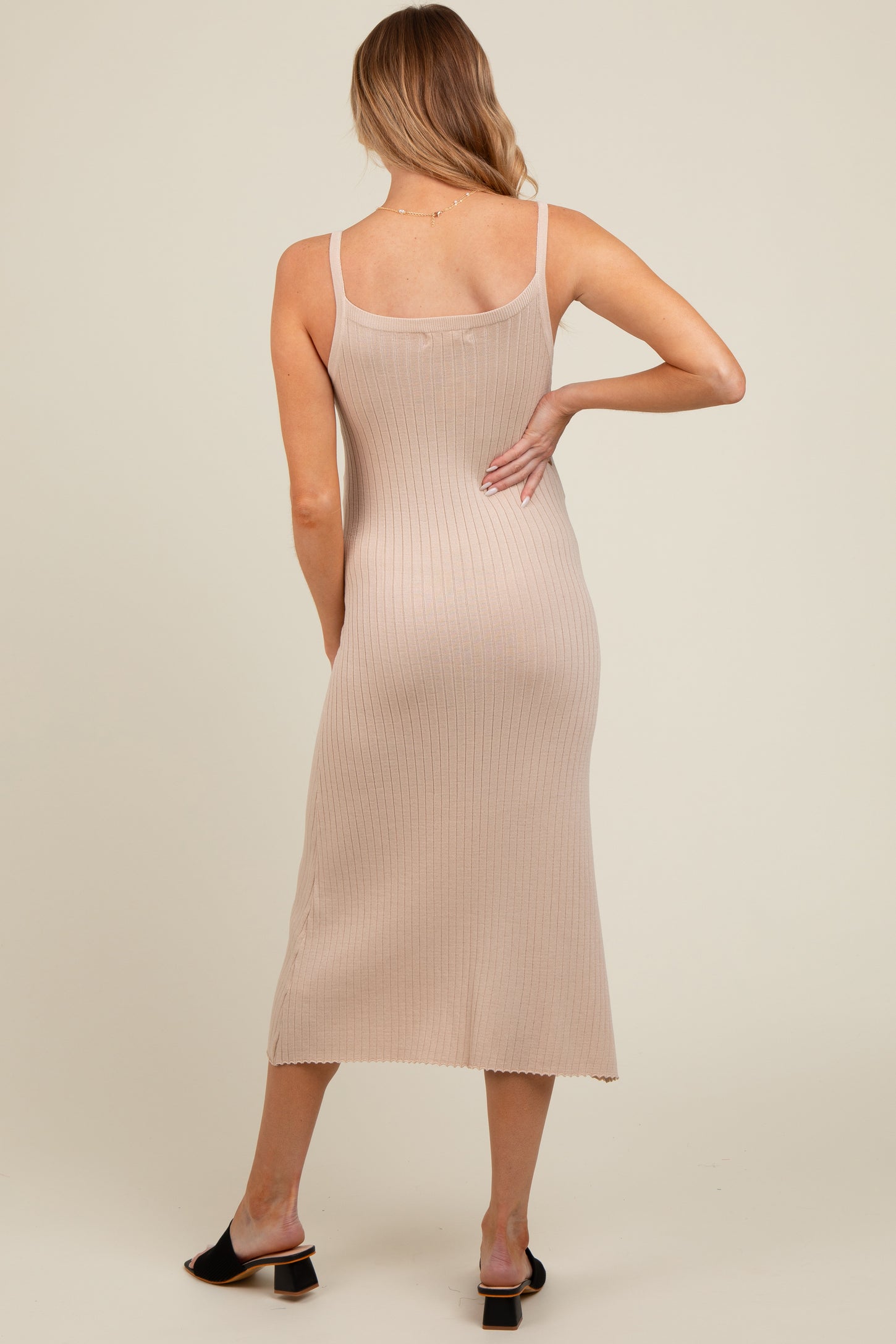 woman wearing a beige ribbed maternity midi dress with a fitted silhouette and spaghetti straps viewed from the back