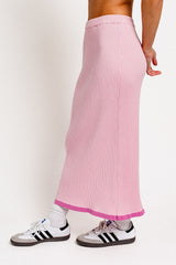 woman wearing a pink ribbed maxi skirt with a pink hem and paired with white and black sneakers