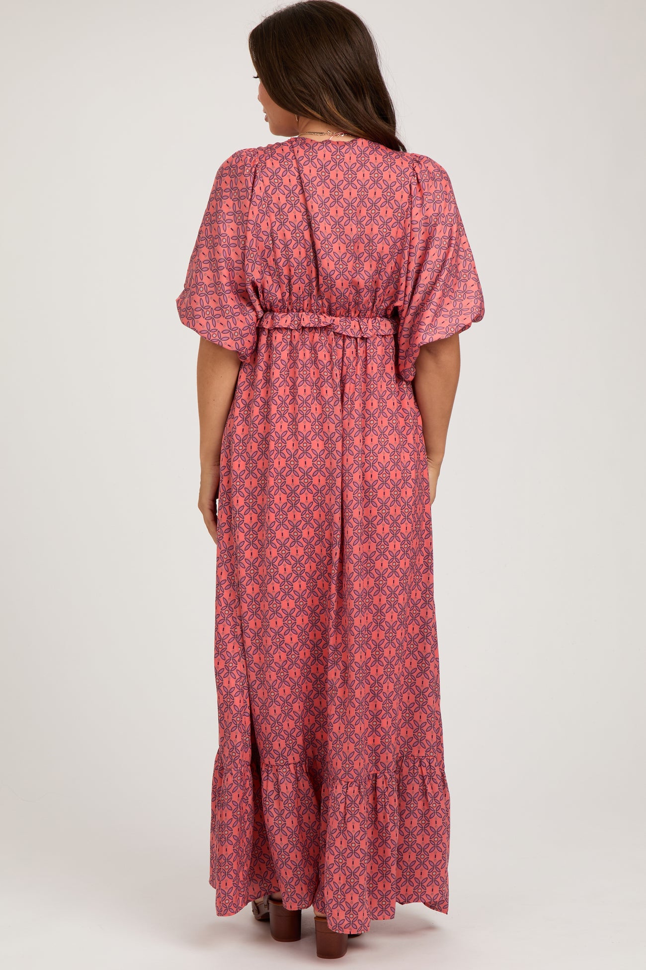 woman wearing a patterned pink maternity maxi dress with a belt and flutter sleeves seen from the back