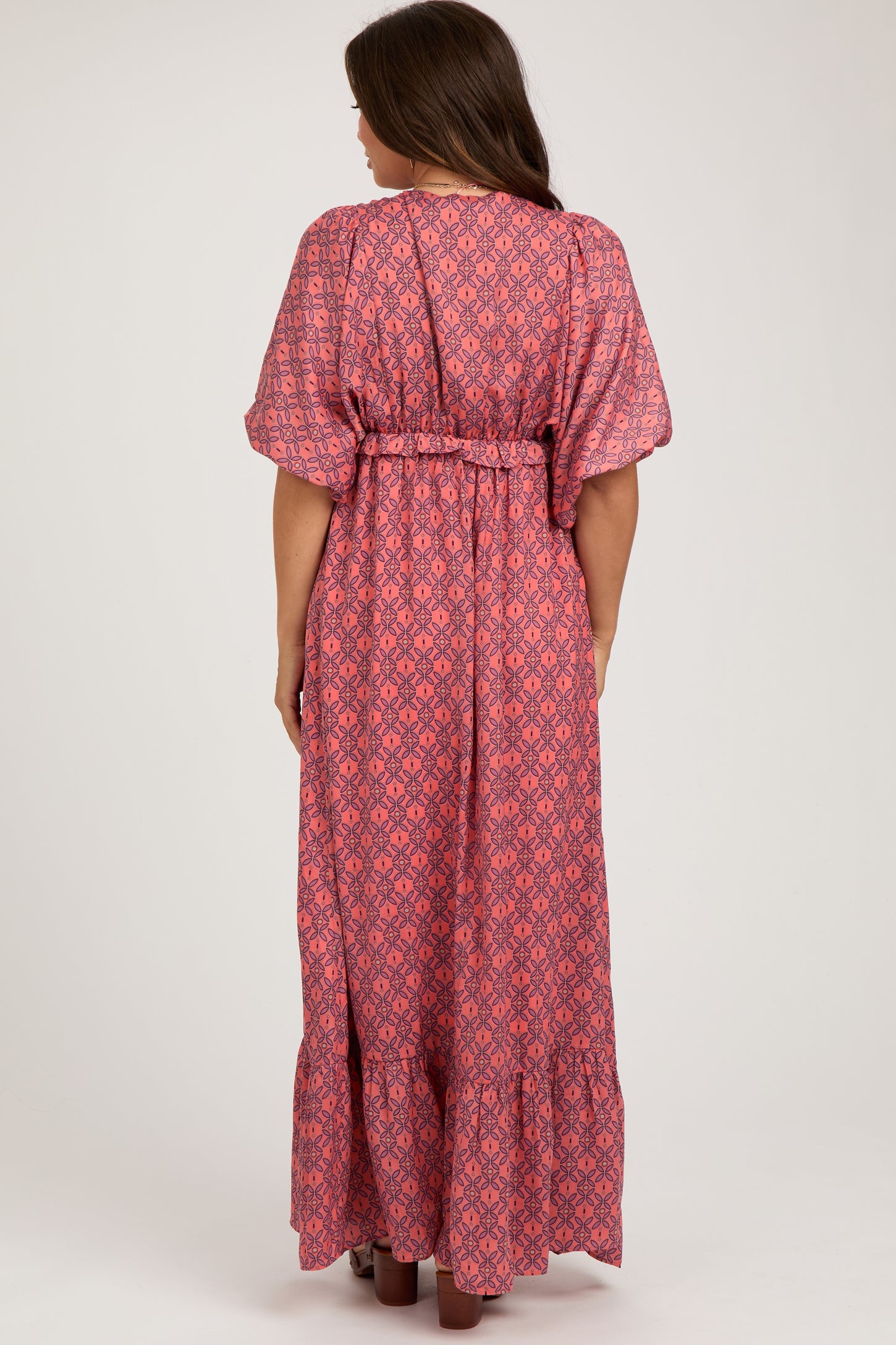 woman wearing a patterned pink maternity maxi dress with a belt and flutter sleeves seen from the back