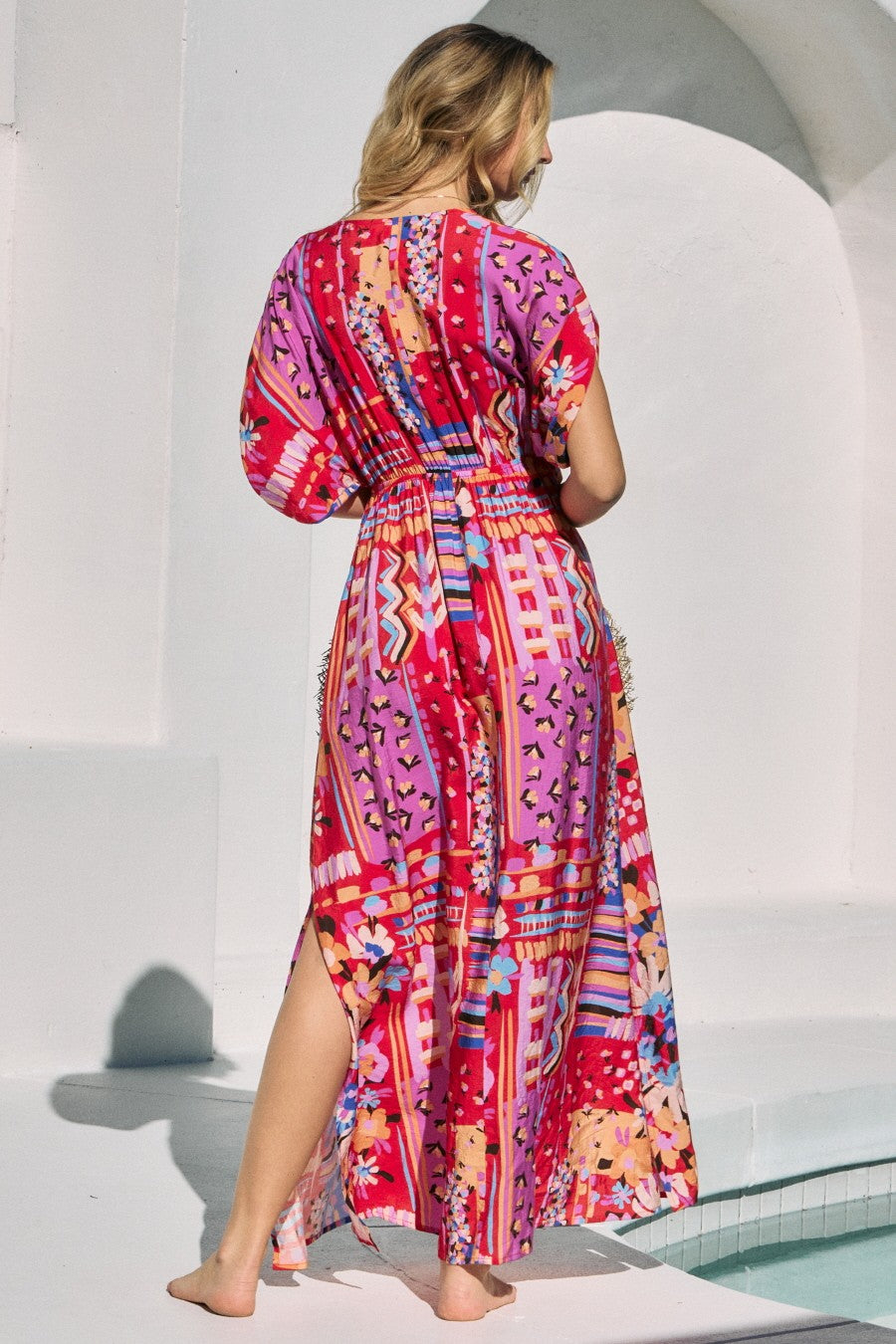woman wearing a colorful, patterned maxi dress with a cinched waist and side slits, shown from the back