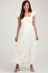 woman wearing a white maternity maxi dress with ruffled sleeves and a smocked bodice, showing her baby bump