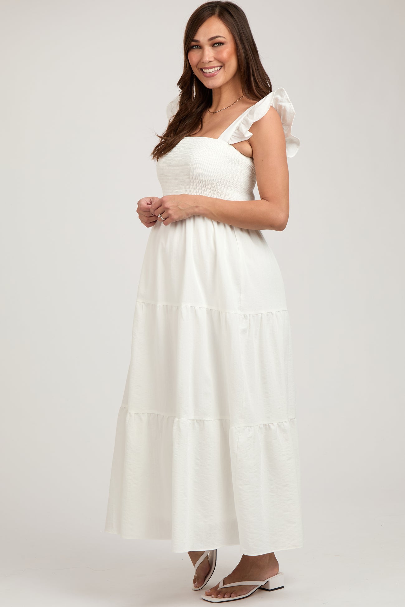 woman wearing a white maternity maxi dress with ruffled sleeves and a fitted smocked bodice