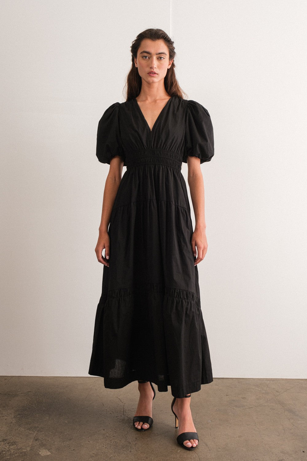 woman wearing a black puff sleeve maxi dress with a deep v-neck and tiered skirt