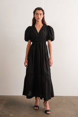 woman wearing a black puff sleeve maxi dress with a deep v-neck and tiered skirt