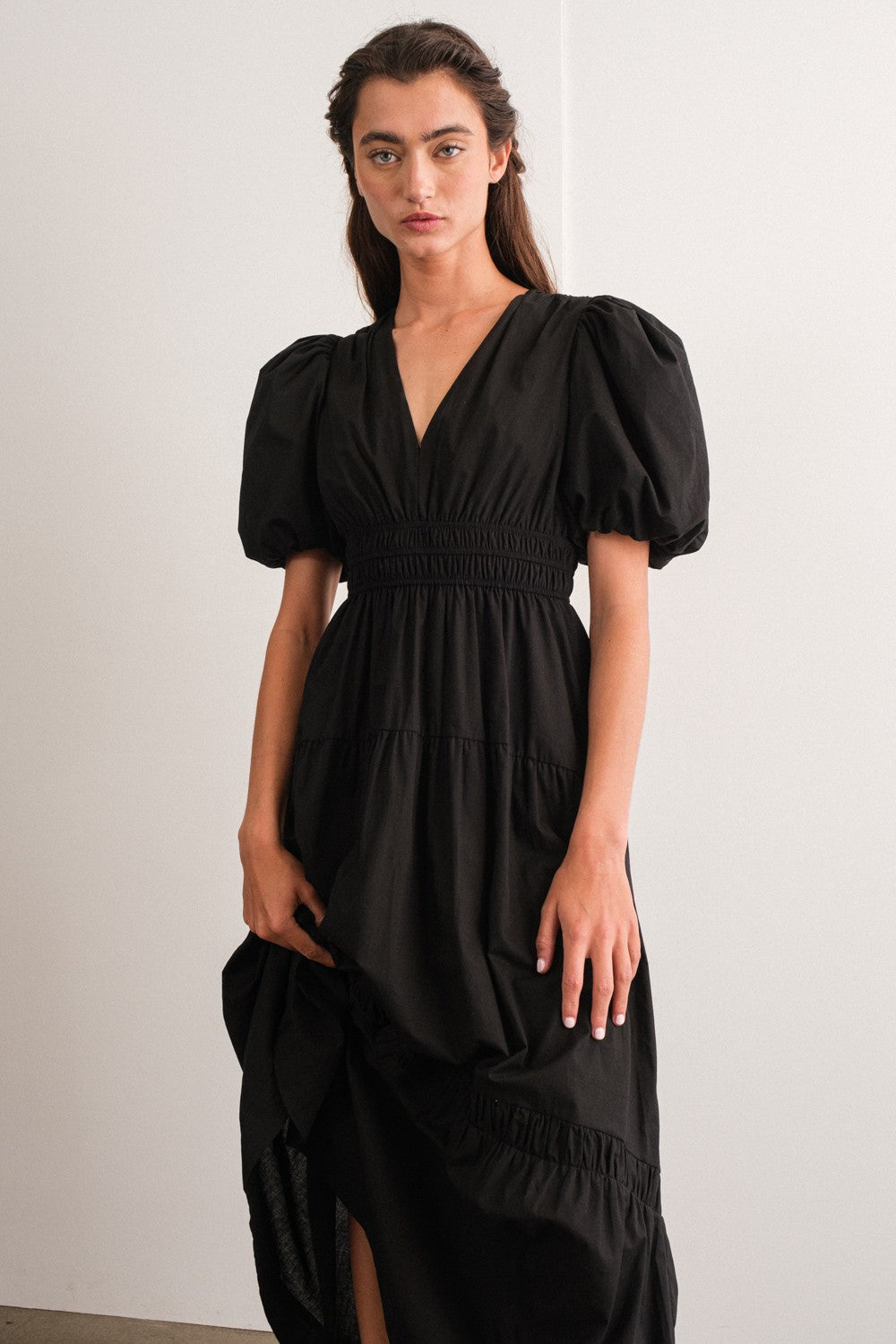woman wearing a black puff sleeve maxi dress with a deep v-neck and smocked waist detail
