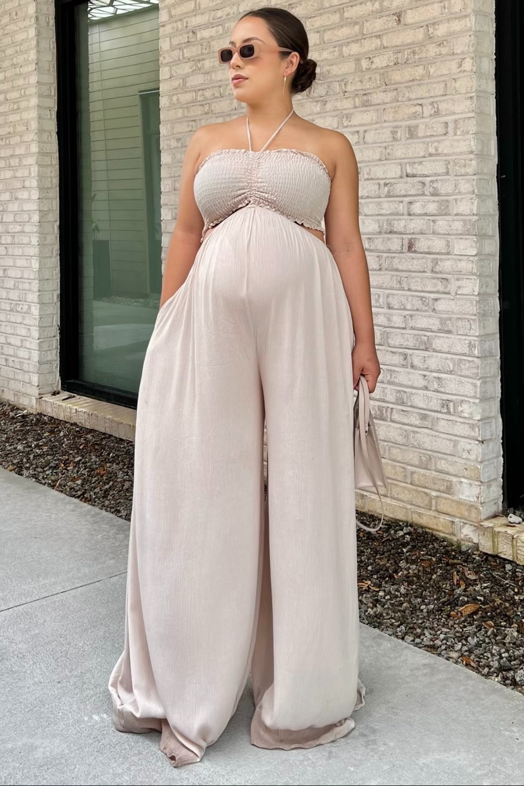 woman wearing a light pink strapless maternity jumpsuit with a smocked bodice and wide legs, showcasing her baby bump