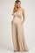 woman wearing a beige maternity jumpsuit with a smocked bandeau top and wide legs, showing her baby bump