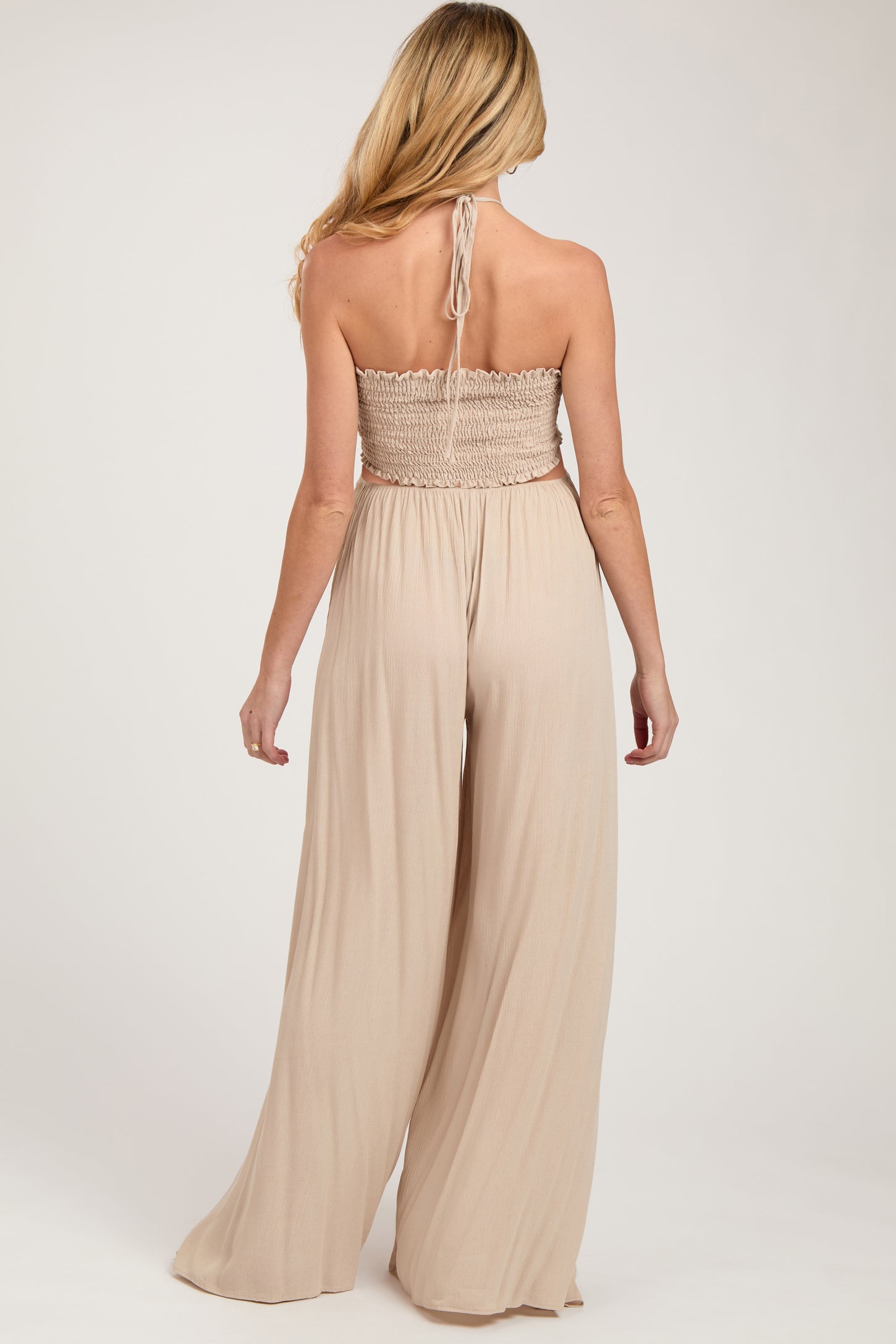 woman wearing a tan maternity jumpsuit with a smocked bodice and wide leg pants, showing her back