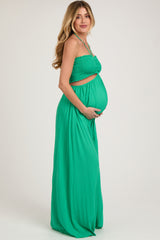 woman wearing a green maternity dress with smocked bodice and holding her baby bump