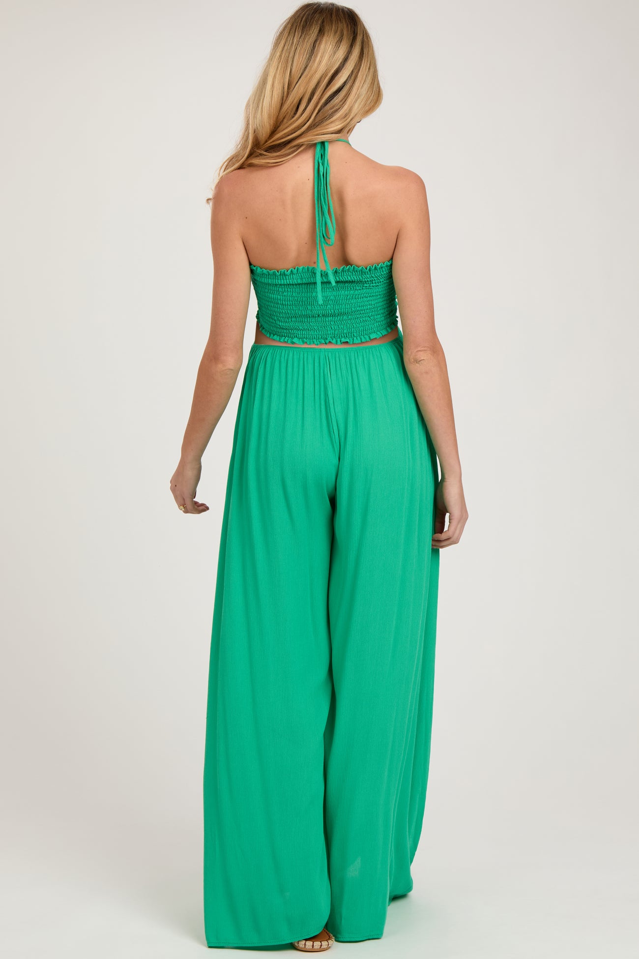 woman wearing a green halter neck maternity jumpsuit with a smocked bodice and wide-leg pants