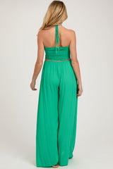 woman wearing a green halter neck maternity jumpsuit with a smocked bodice and wide-leg pants