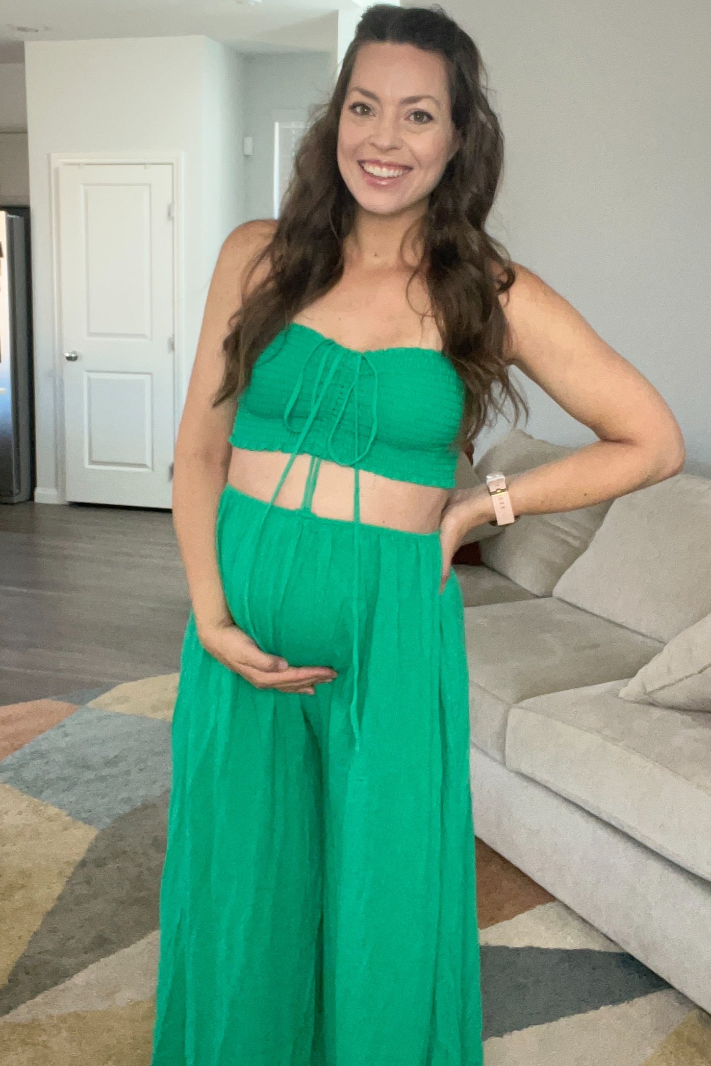 woman wearing a green maternity two-piece outfit with a cropped top and wide-leg pants, holding her baby bump
