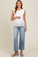 woman wearing a white ruffled maternity tank top and blue wide-leg jeans, holding her baby bump