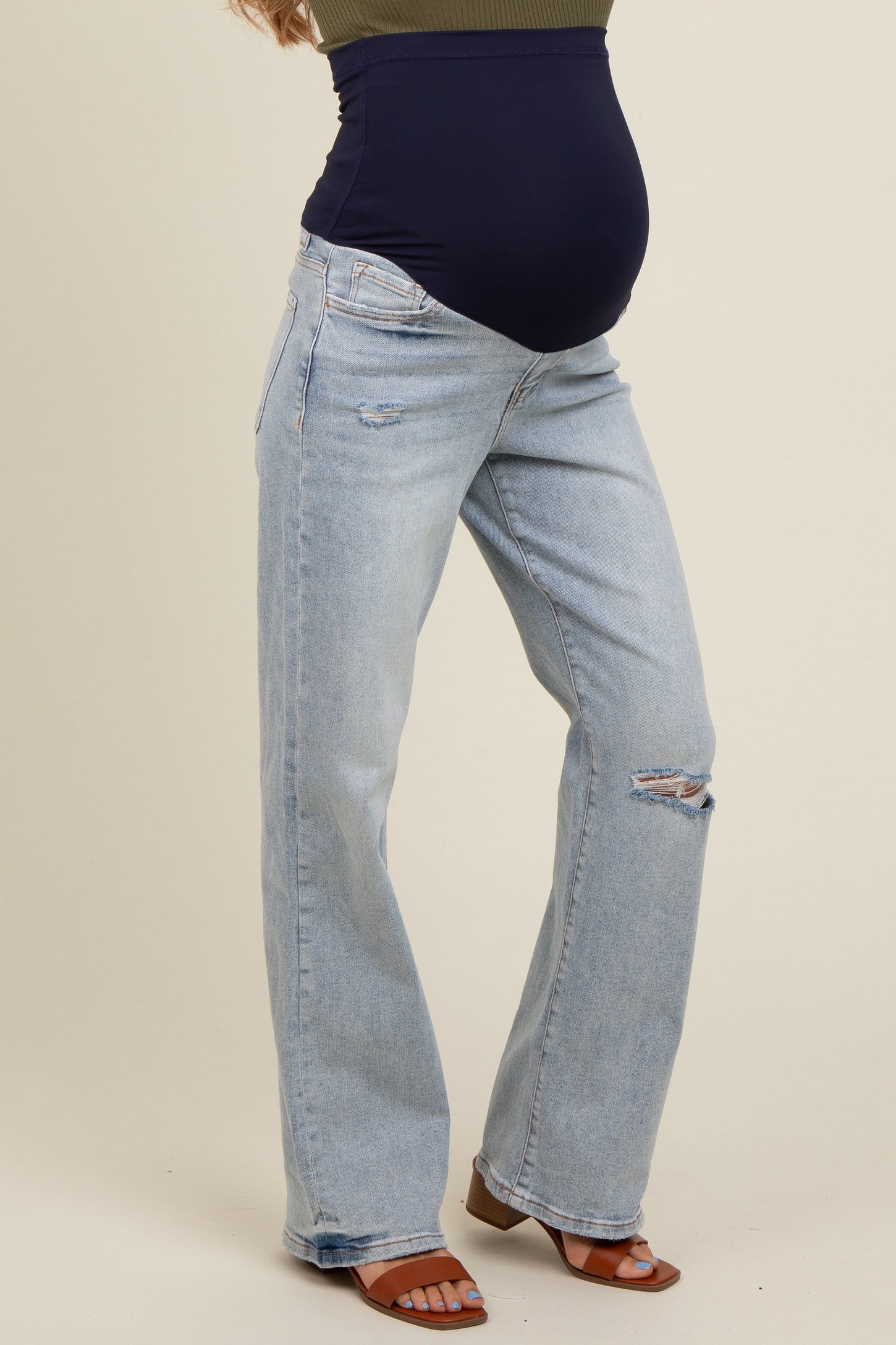 woman wearing a dark blue maternity top and light wash distressed flared jeans, showing her baby bump