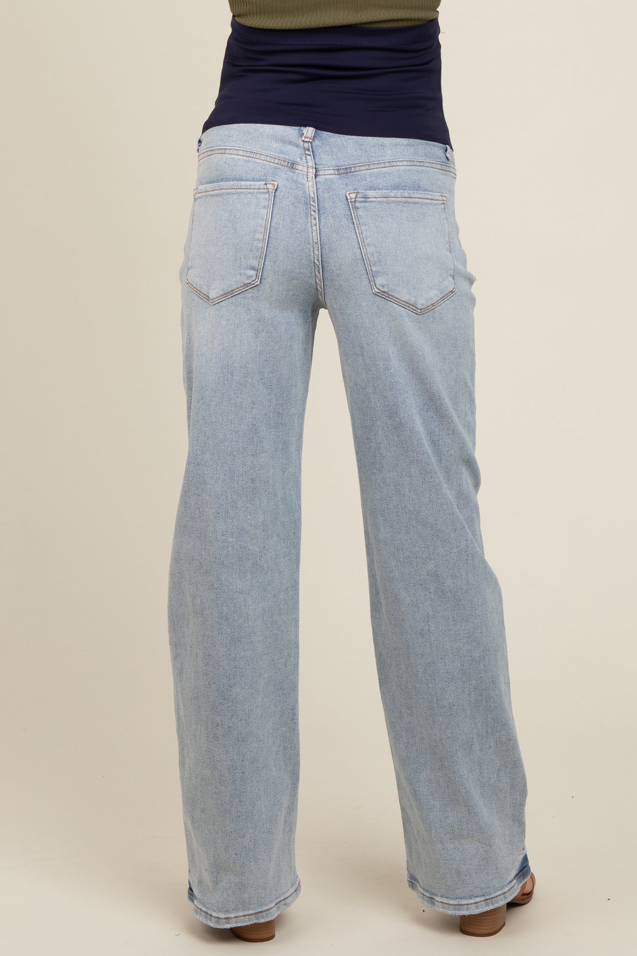 woman wearing light blue maternity jeans, seen from the back with a fitted top underneath the waistband