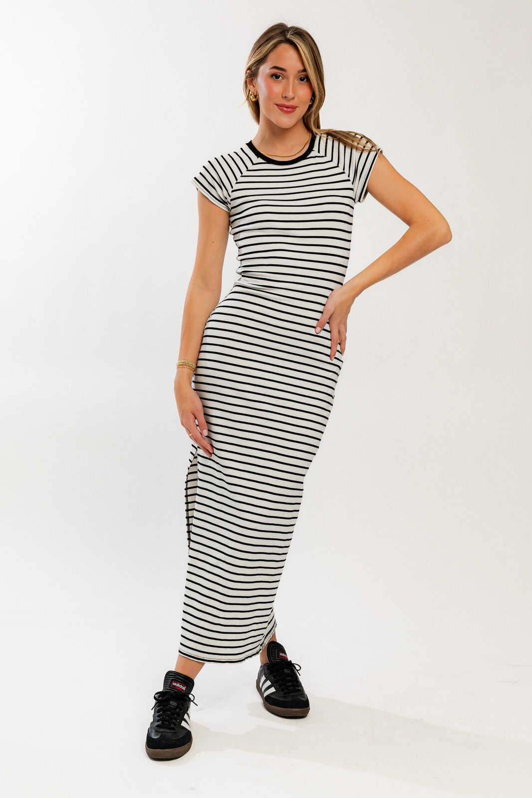 woman wearing a black and white striped maxi dress with short sleeves and side slits, posing with one hand on her hip