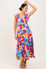 woman wearing a colorful floral maxi dress with ruffle sleeves and a tiered skirt, posing playfully
