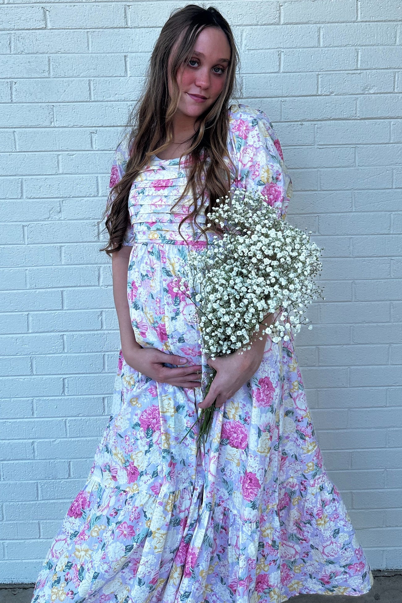 woman wearing a floral maternity maxi dress and holding a bouquet of baby’s breath with a visible baby bump