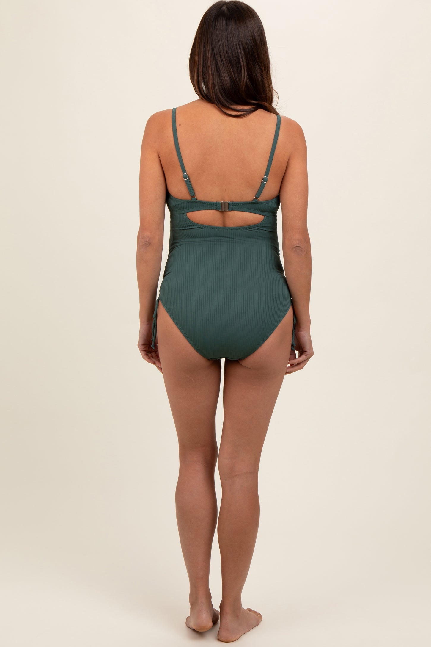 woman wearing a dark green ribbed maternity swimsuit with adjustable straps and a cutout back, showing her baby bump