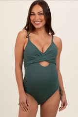 woman wearing a forest green maternity swimsuit with a cross front design and side ties, showcasing her baby bump