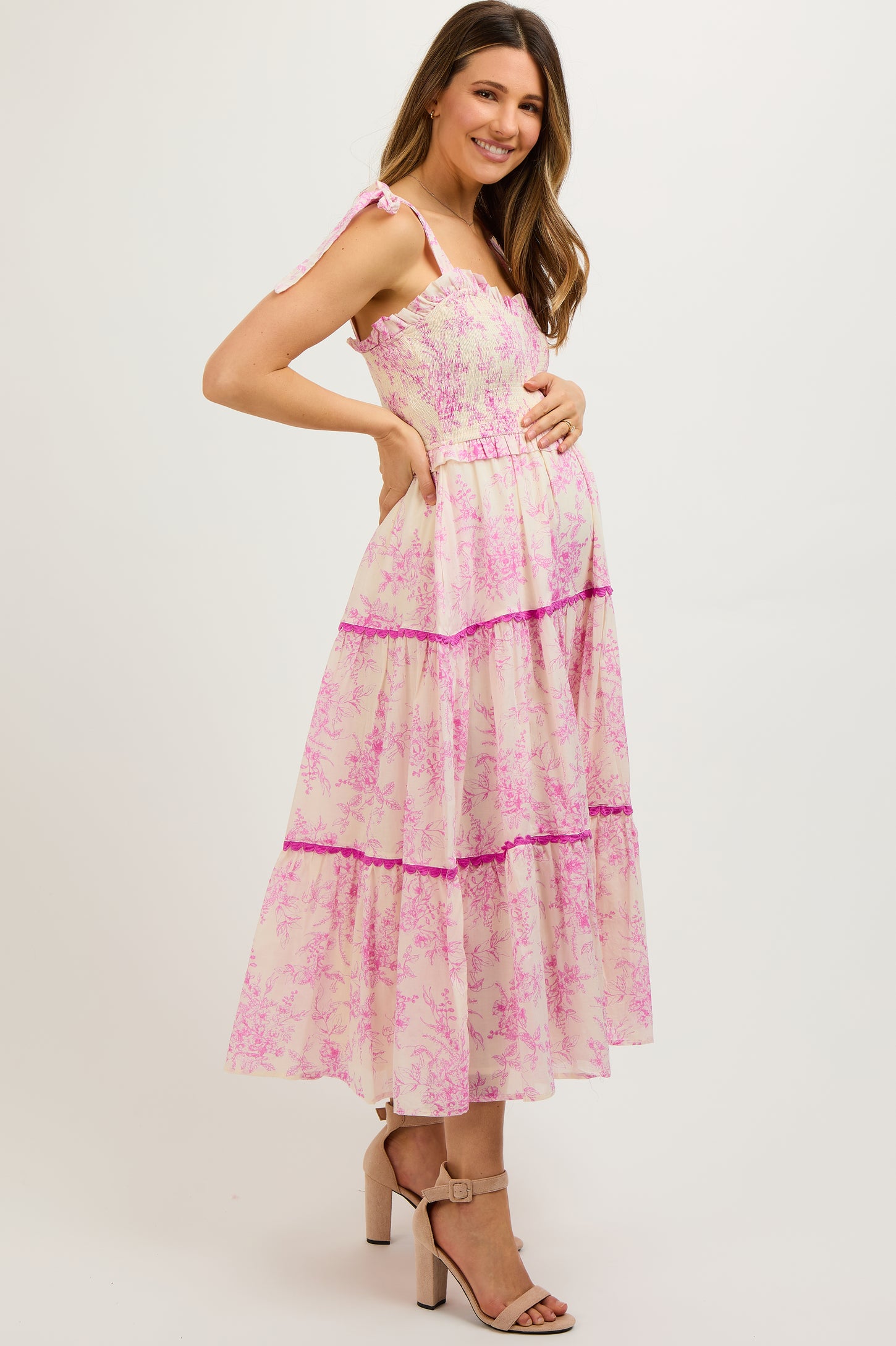 woman wearing a pink floral maternity maxi dress with ruffles and a visible baby bump
