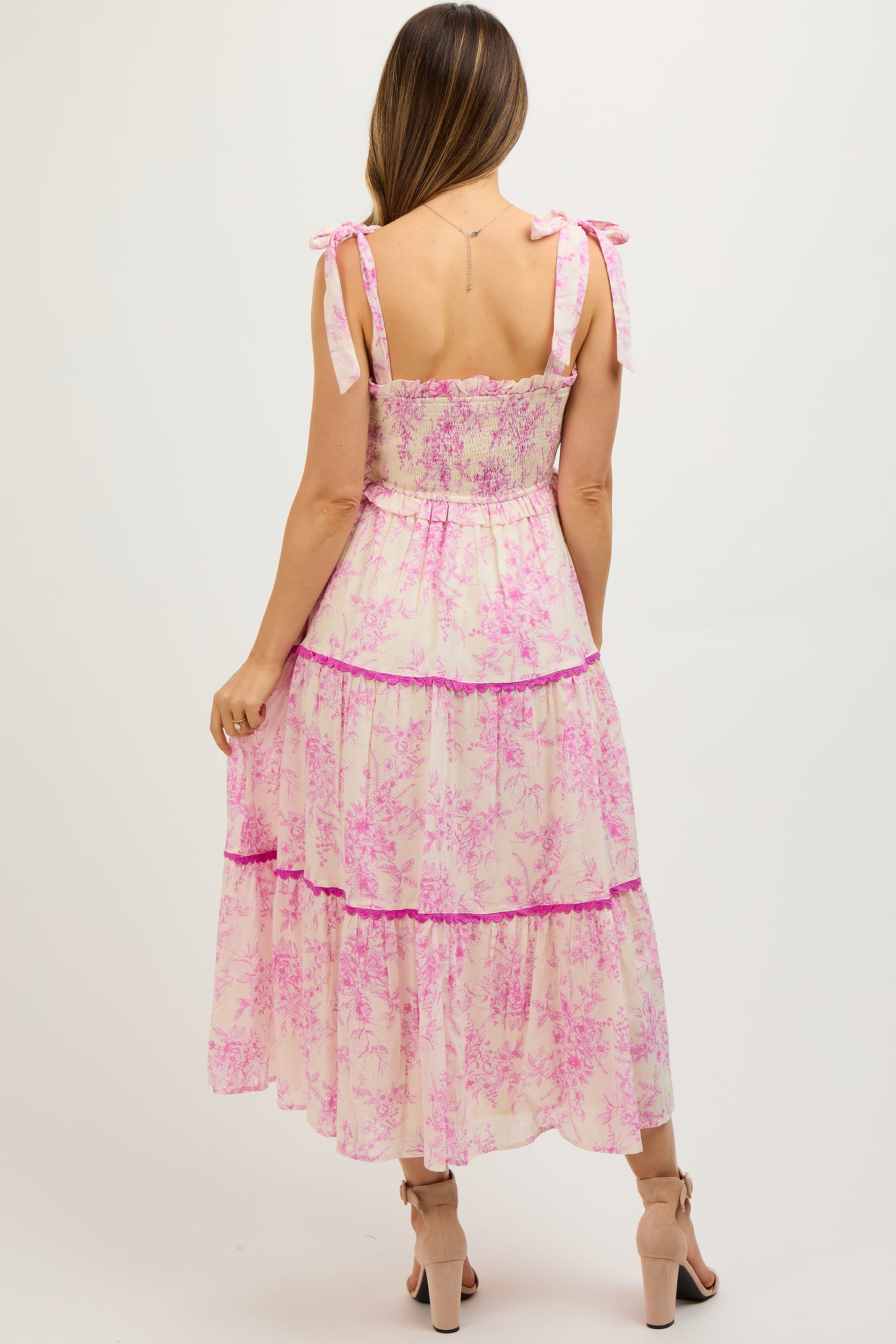 woman wearing a pink floral maternity maxi dress with tie straps and a tiered design, showing her baby bump
