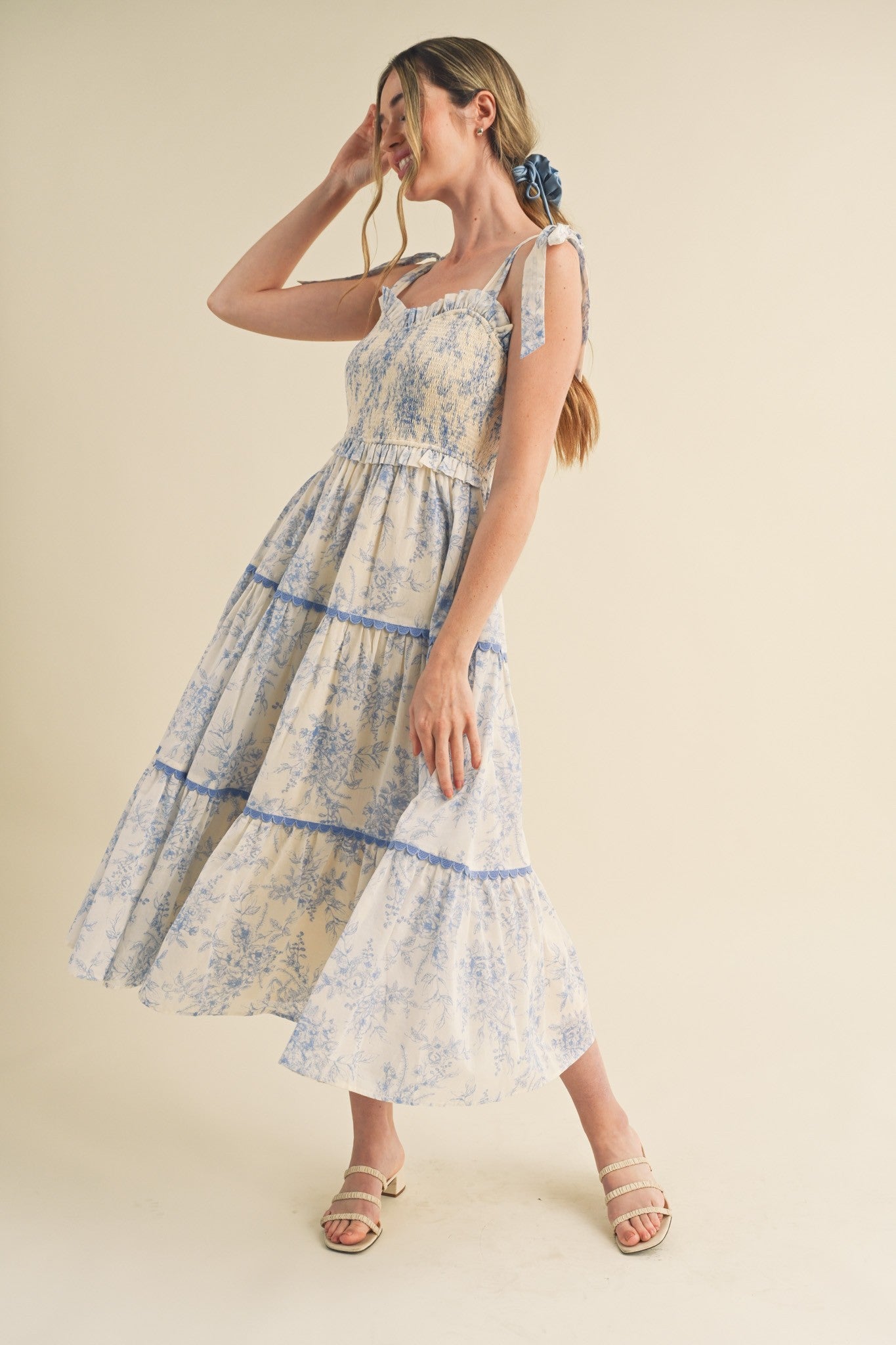 woman wearing a floral print maxi dress with blue and white tones, tied straps, and a flowing skirt