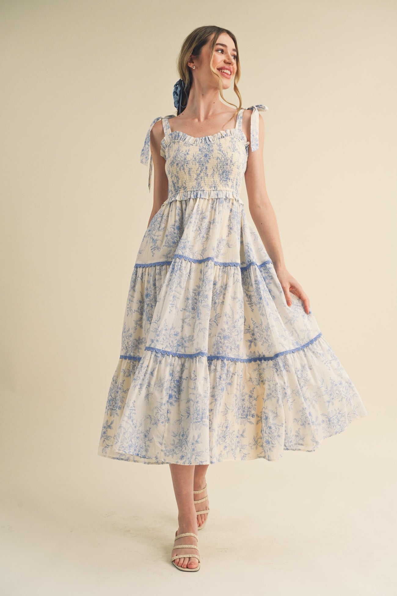 woman wearing a floral print maxi dress with blue accents and tie straps, standing and smiling