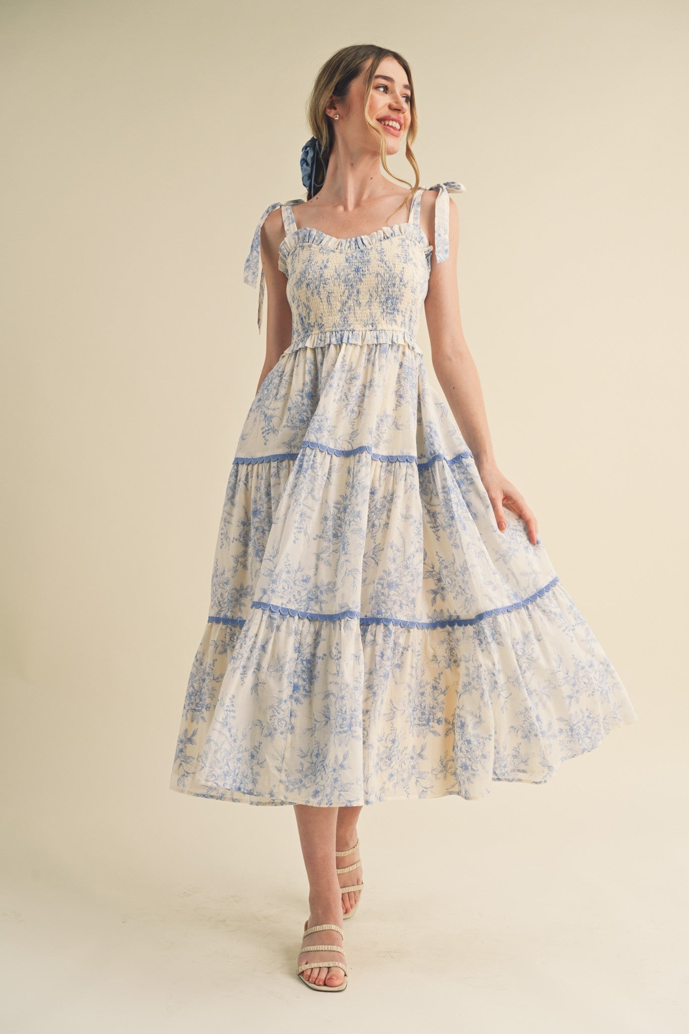 woman wearing a floral print maxi dress with blue accents and tie straps, standing and smiling