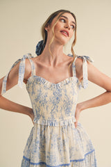 woman wearing a light blue and cream floral print sundress with ruffled layers and adjustable tie straps
