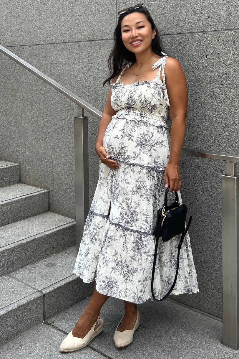 woman wearing a floral print maternity dress with a tiered skirt and holding her baby bump while standing on stairs