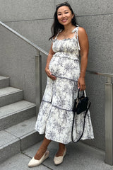 woman wearing a floral print maternity dress with a tiered skirt and holding her baby bump while standing on stairs