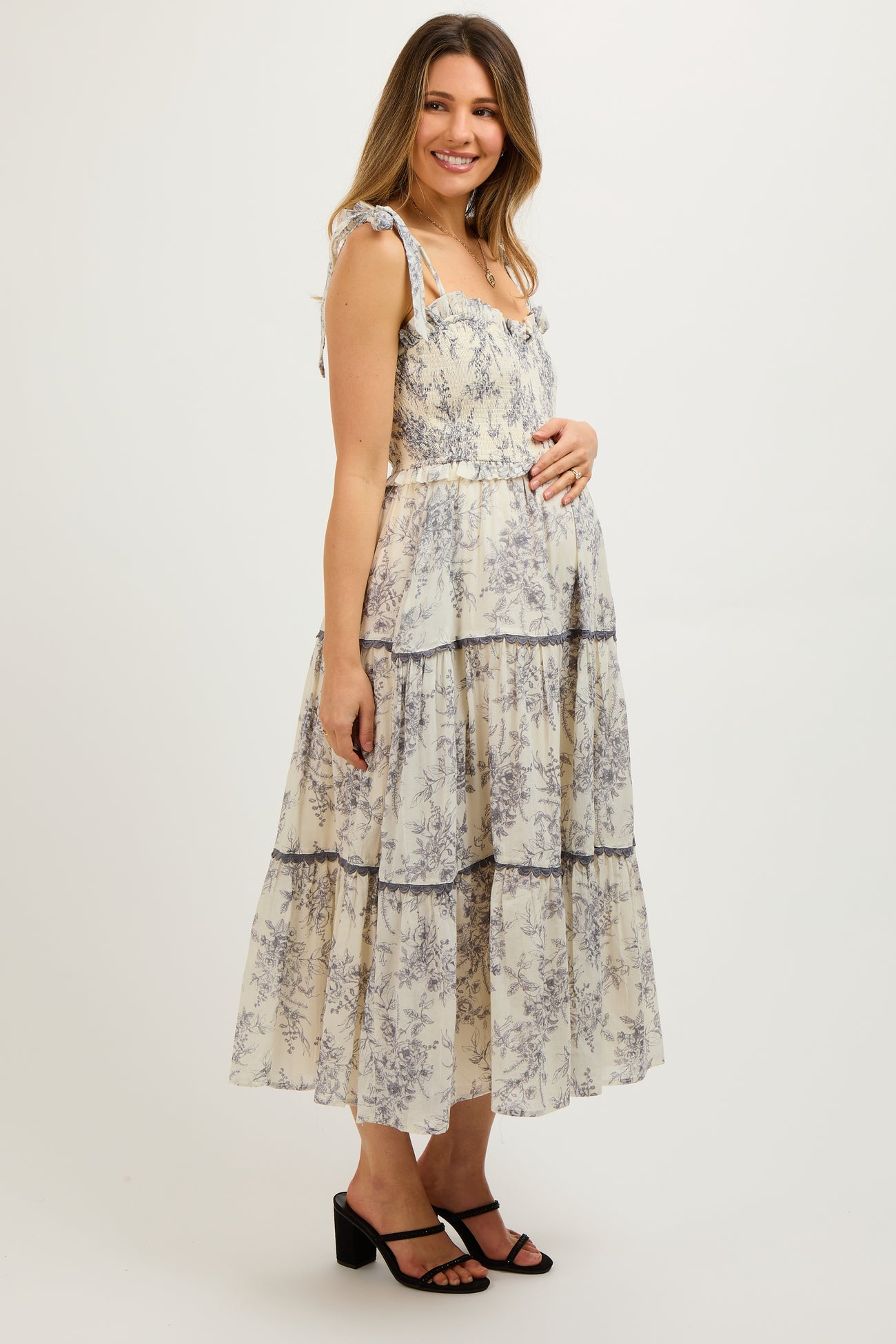woman wearing a cream floral print maternity tiered maxi dress with ruffled straps and a visible baby bump