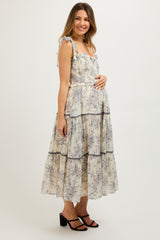 woman wearing a cream floral print maternity tiered maxi dress with ruffled straps and a visible baby bump