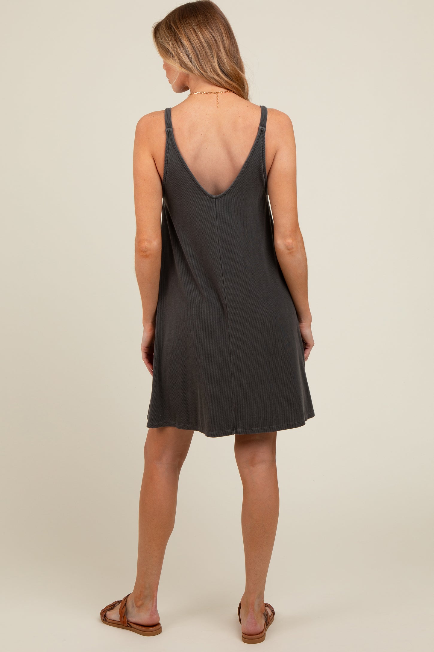 woman wearing a dark gray sleeveless maternity dress with a v-back design, shown from the back