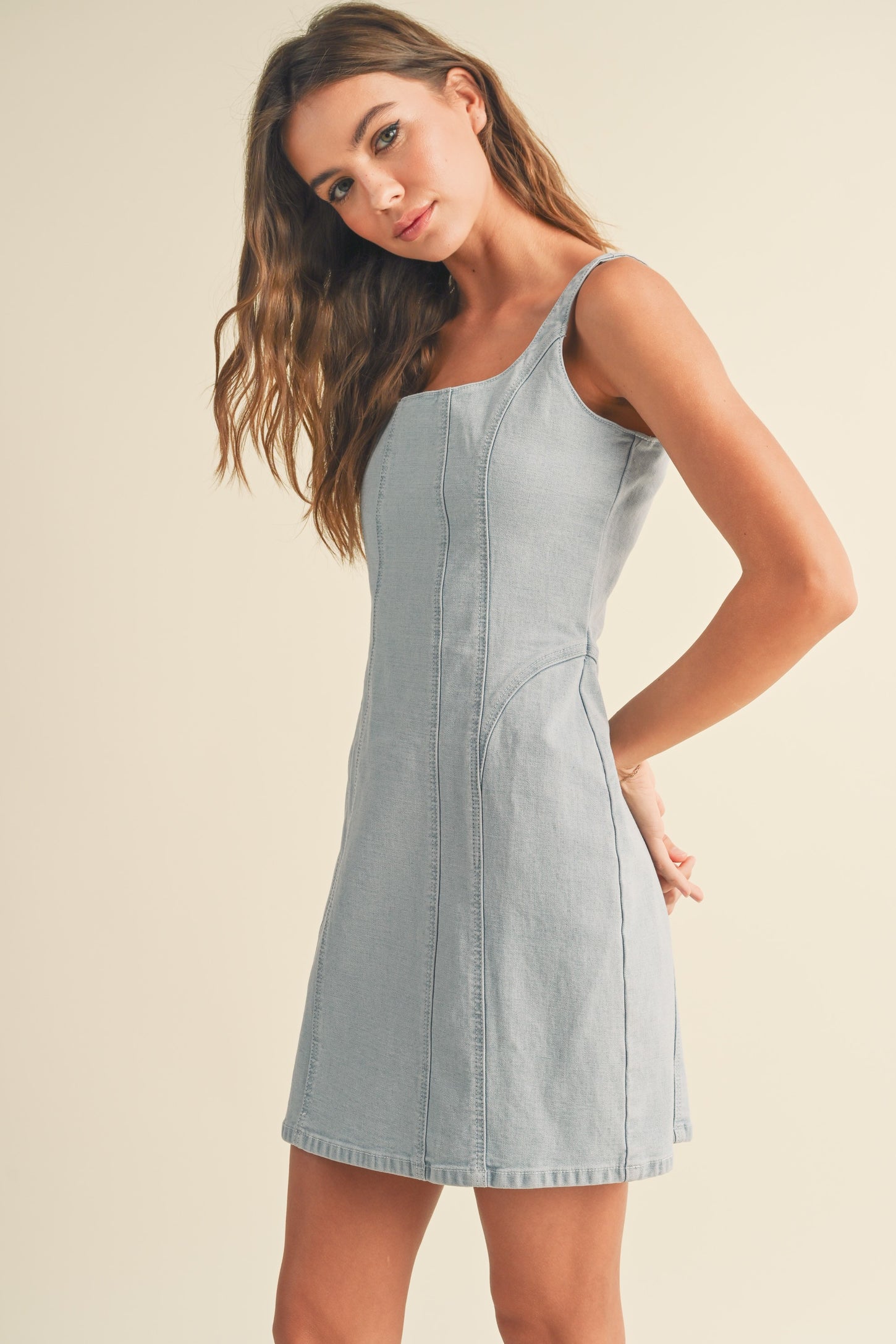 woman wearing a light blue sleeveless denim dress with side seams and a fitted style