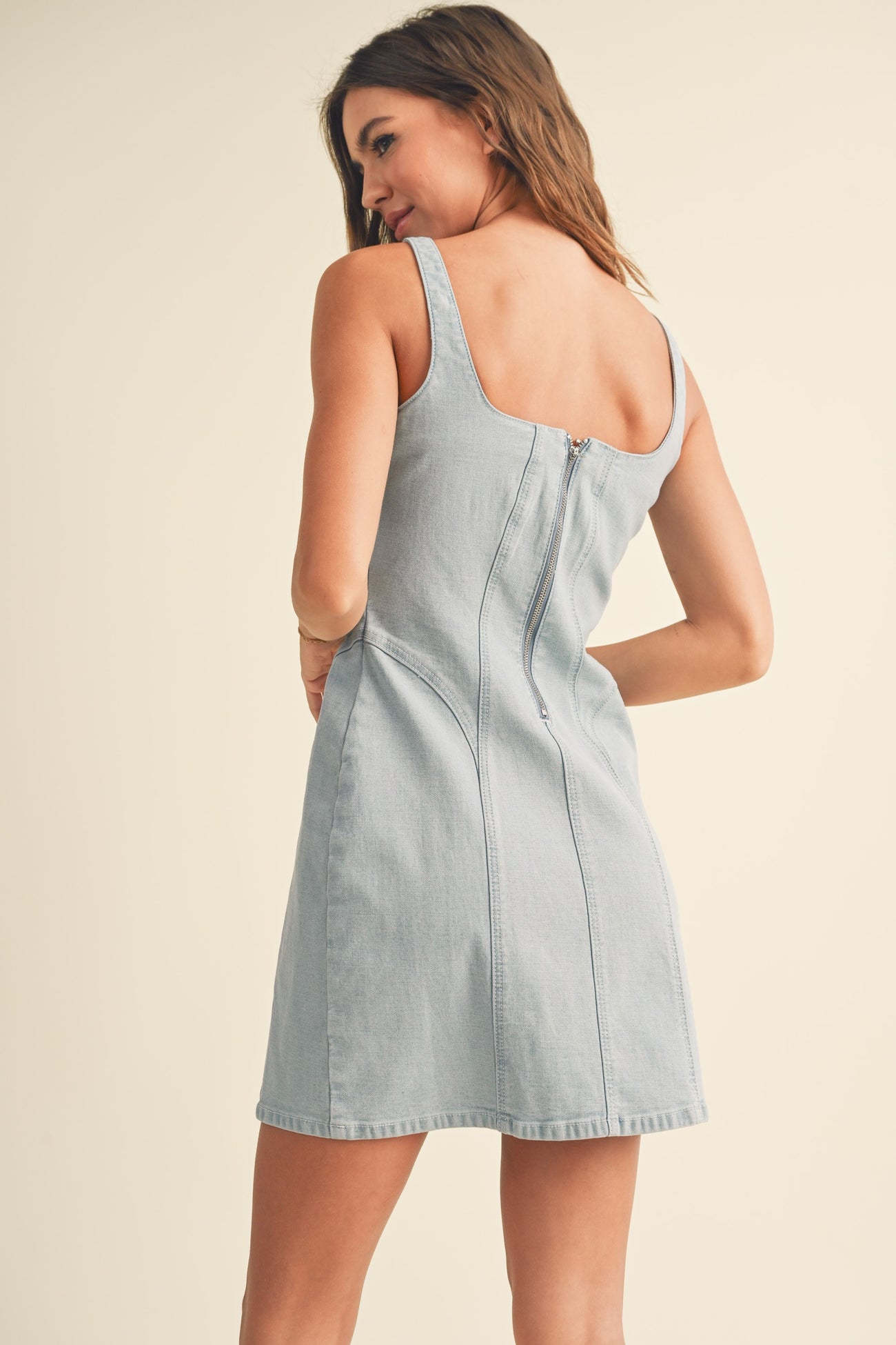 woman wearing a light blue denim mini dress with a square neckline and a zip closure at the back