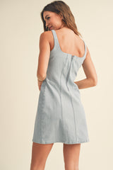 woman wearing a light blue denim mini dress with a square neckline and a zip closure at the back