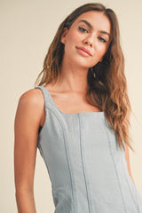 woman wearing a light blue fitted denim dress with wide shoulder straps and seam detailing