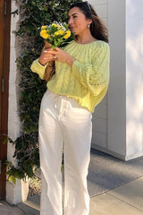 woman wearing a light yellow sweater with knit details and white wide-leg pants, holding a bouquet of flowers