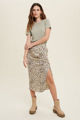 woman wearing a green short sleeve top and a leopard print midi skirt with a slit, paired with beige ankle boots