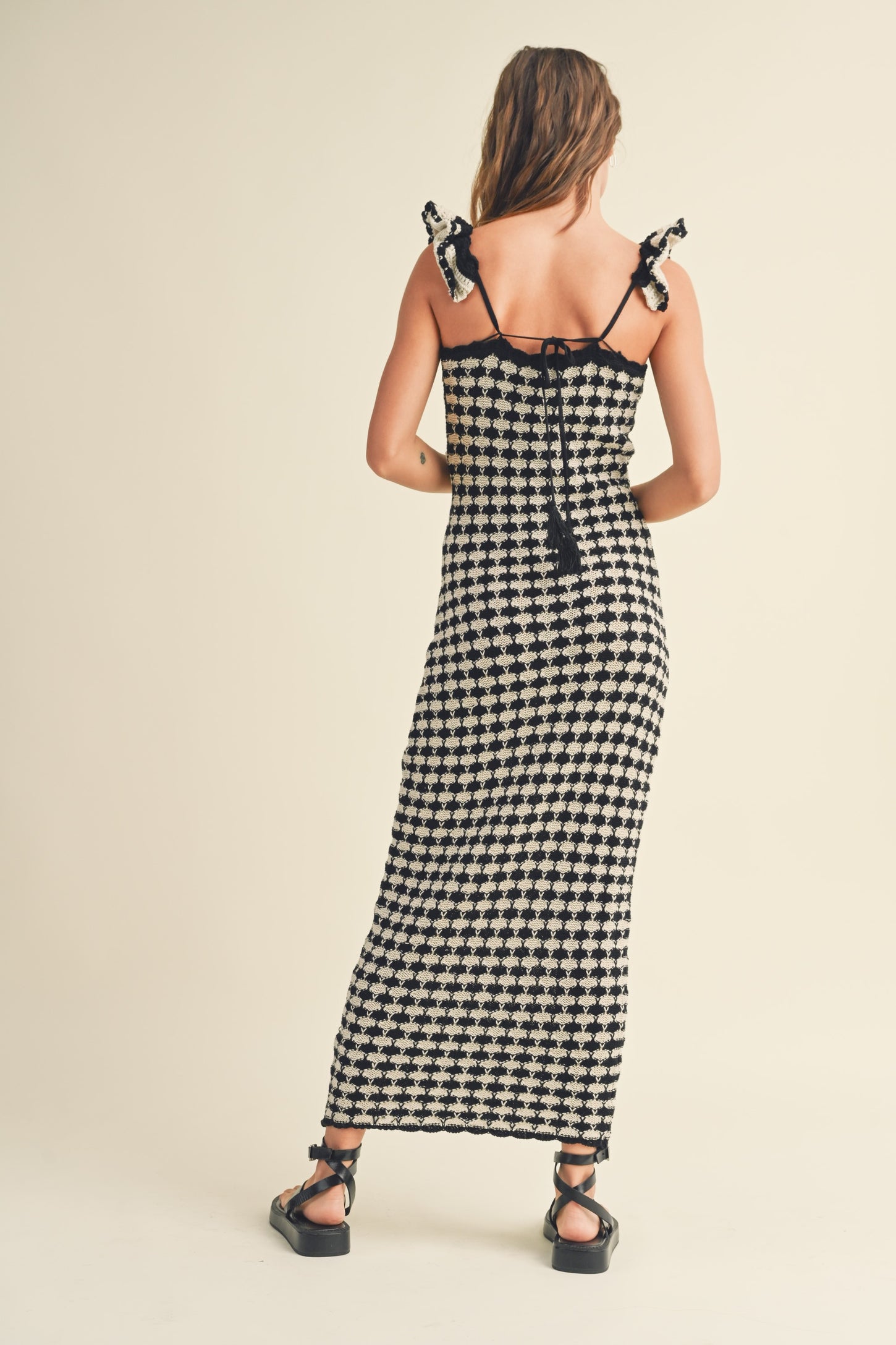 woman wearing a black and white checkered maxi dress with shoulder ties and a fitted bodice from the back